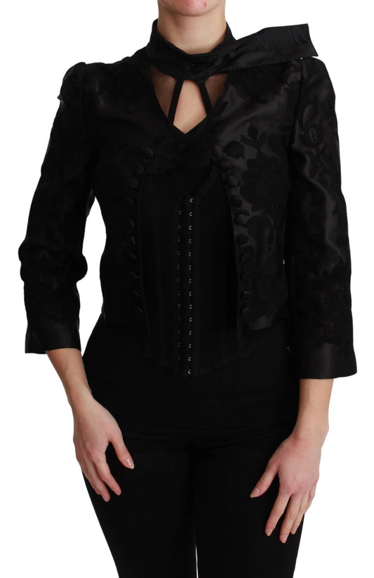 Woman wearing a black embroidered cropped jacket with decorative buttons and high collar
